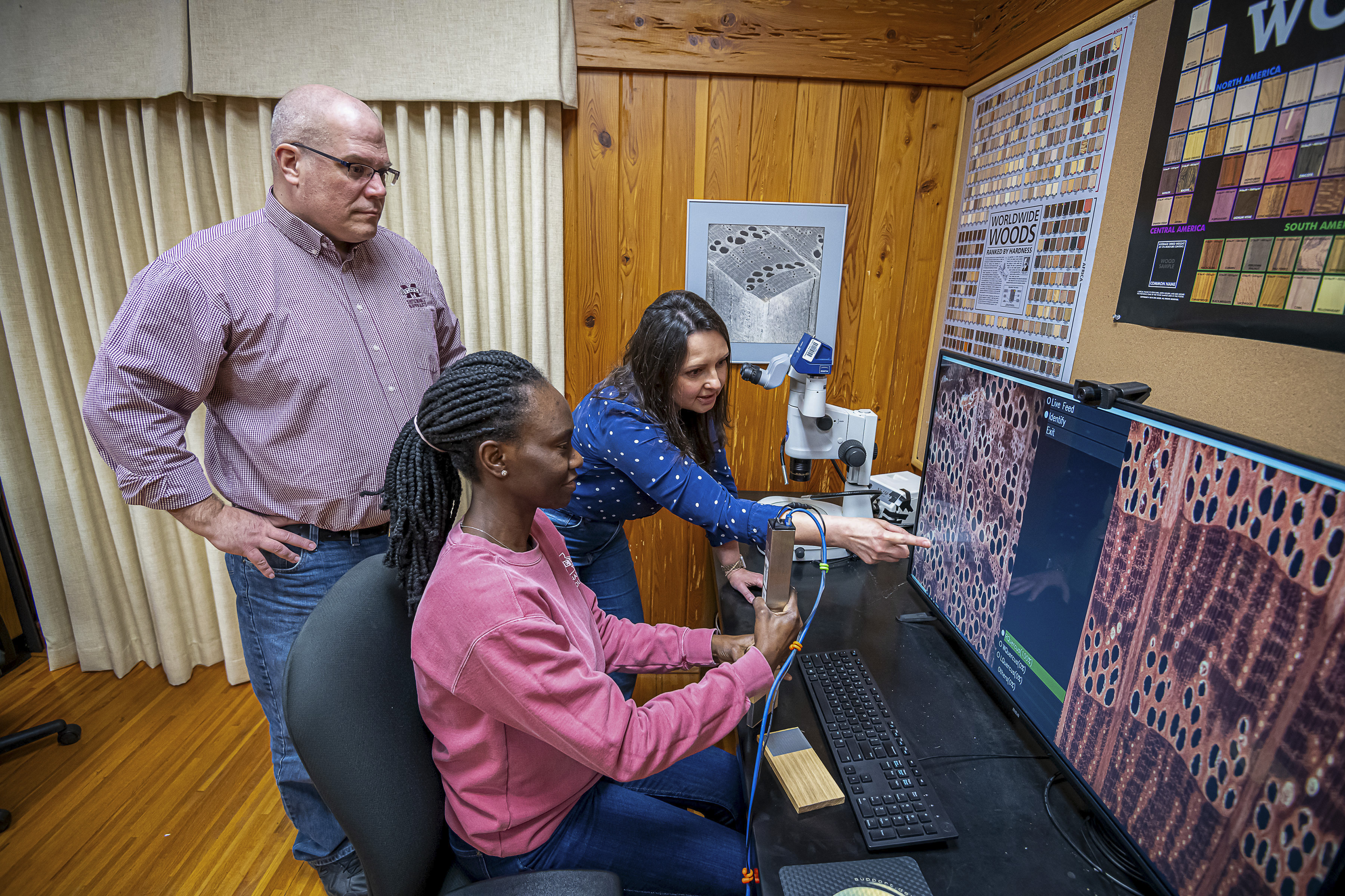 A man and two women look at a computer screen to identify a wood species. 