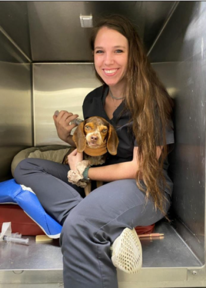 Veterinary Technician holding a dog and smiling at the camera.